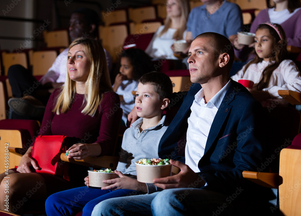 Family with son watching movie and eating popcorn in cinema hall