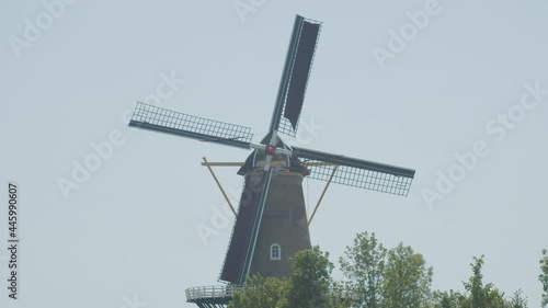 Medium shot of classical Dutch windmill with spinning blades. Tourists are walking around on the buildings deck photo