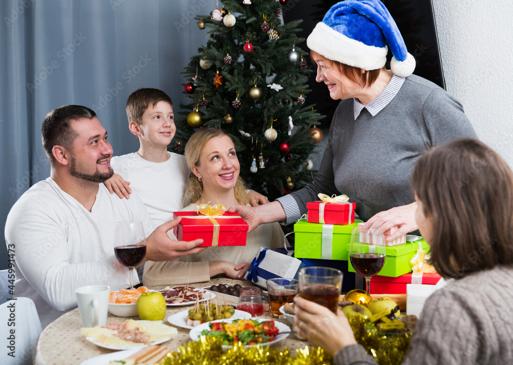 Happy grandma giving Christmas presents to children and grandson during dinner at home