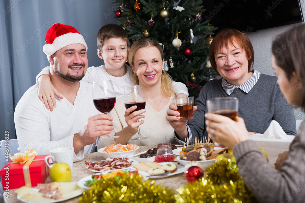 Cheerful family at dining table for Christmas dinner against backdrop of decorated fir tree