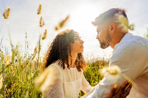 Romantic scene of multiracial passionate young couple in love looking in eyes each other among high grass vegetation at sunset or dawn with sun backlit effect Romance dream shot of lovers in nature