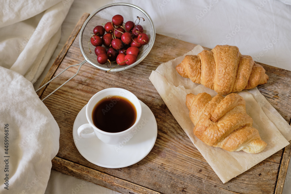 Tasty breakfast with fresh croissant, coffee, cherries on a wooden tray. Espresso on a breakfast tray