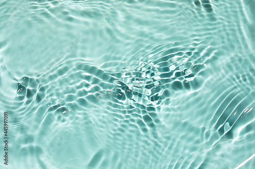 Trendy summer exotic background. Blurred or defocused transparent clear water waves in sunlight. Green liquid colored clear water surface texture with splashes bubbles. 