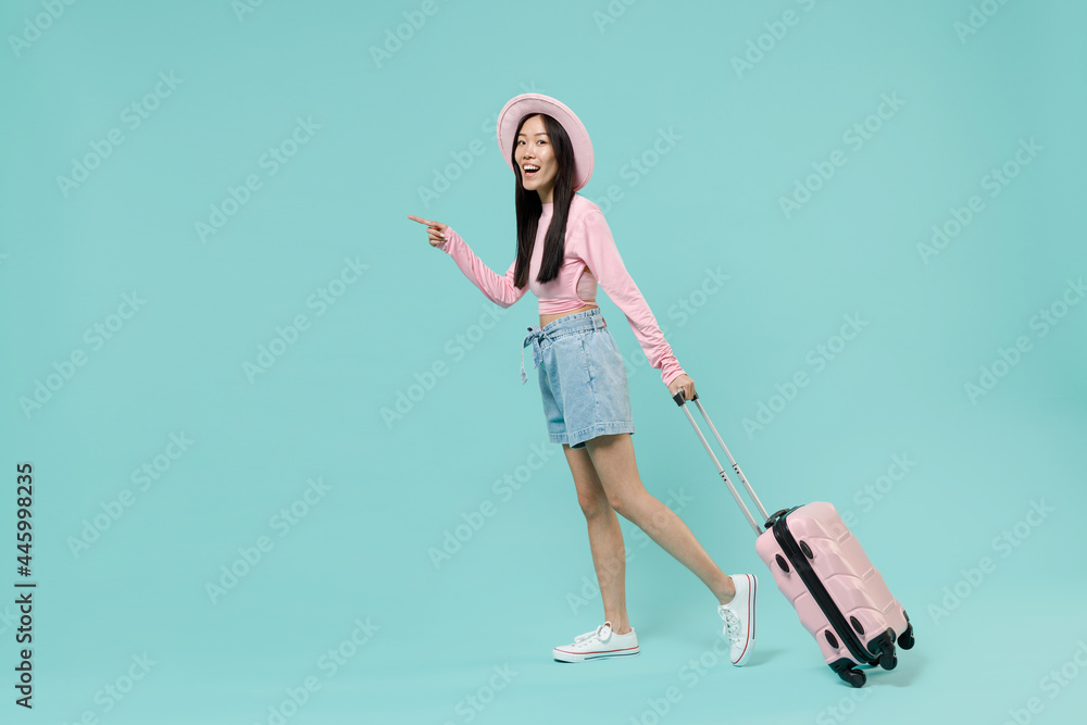 Full size body traveler tourist asian woman wear pink casual clothes hat hold suitcase bag isolated on pastel pink color background studio. Passenger travel abroad getaway. Air flight journey concept. Full size body traveler tourist asian woman wear pink casual clothes hat hold suitcase bag isolated on pastel pink color background studio. Passenger travel abroad getaway. Air flight journey concept.