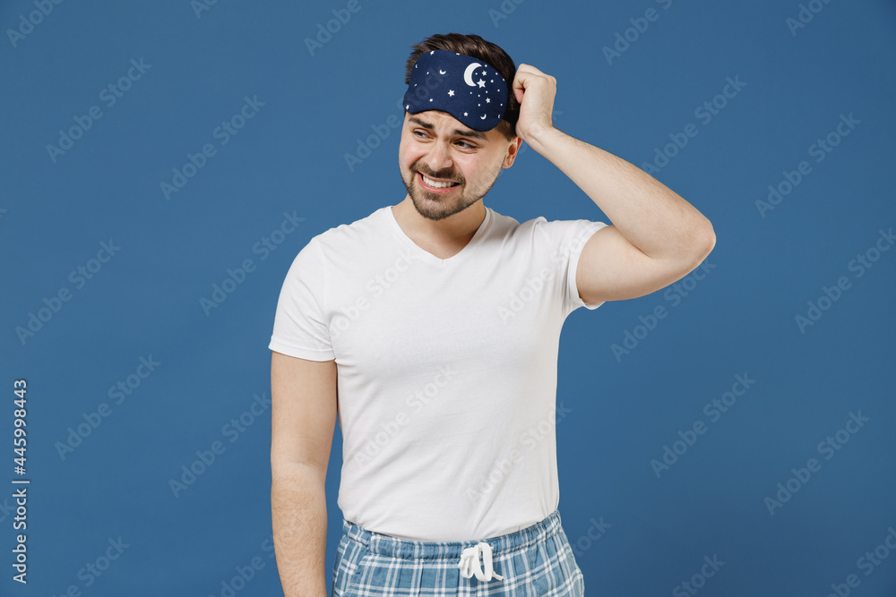Young confused sad puzzled troubled man 20s in pajamas jam sleep mask white t-shirt rest relax at home look aside scratch hold head isolated on dark blue background Bad mood night bedtime concept Young confused sad puzzled troubled man 20s in pajamas jam sleep mask white t-shirt rest relax at home look aside scratch hold head isolated on dark blue background Bad mood night bedtime concept