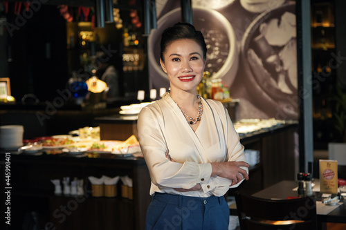 Portrait of happy smiling elegant middle-aged woman standing at bar counter of restaurant she is opening