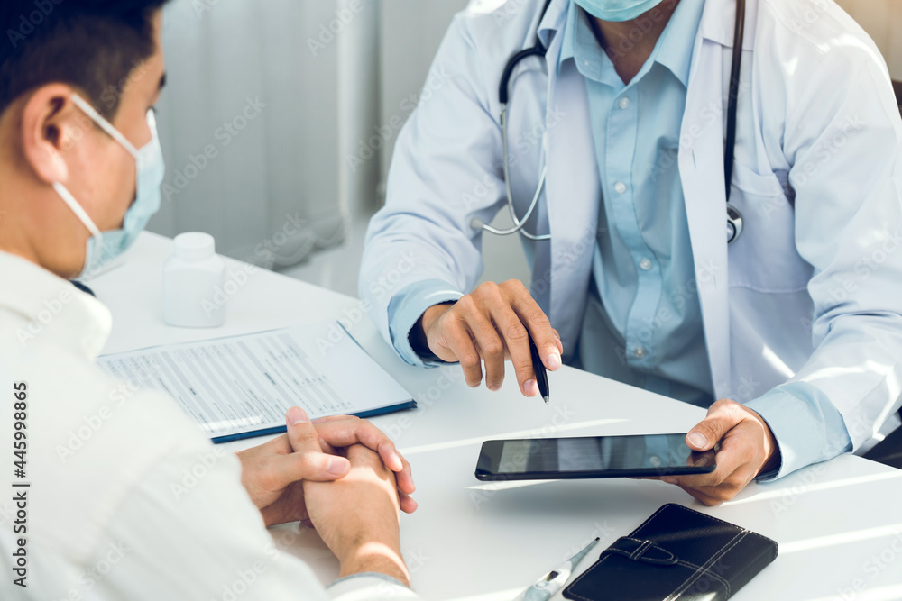 Doctors are explaining the treatment of a sick patient in tablets while wearing a mask during the virus outbreak. Doctors are explaining the treatment of a sick patient in tablets while wearing a mask during the virus outbreak.