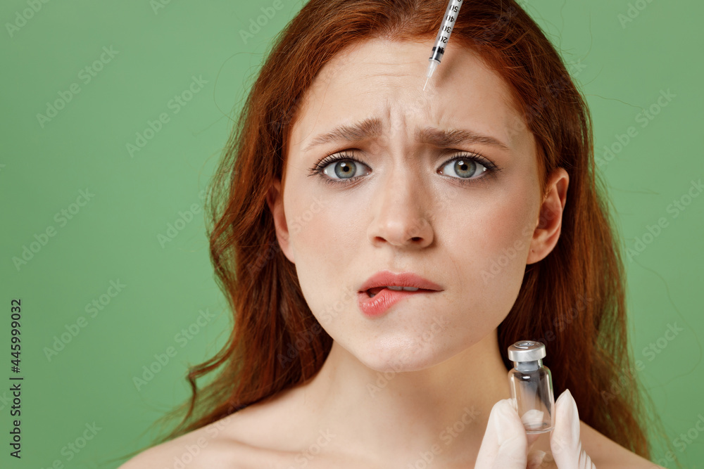 Obraz premium Close up half naked topless redhead woman nude make up visit doctor making mesotherapy injection biting lip isolated on pastel green color background. Skin care healthcare cosmetic procedures concept