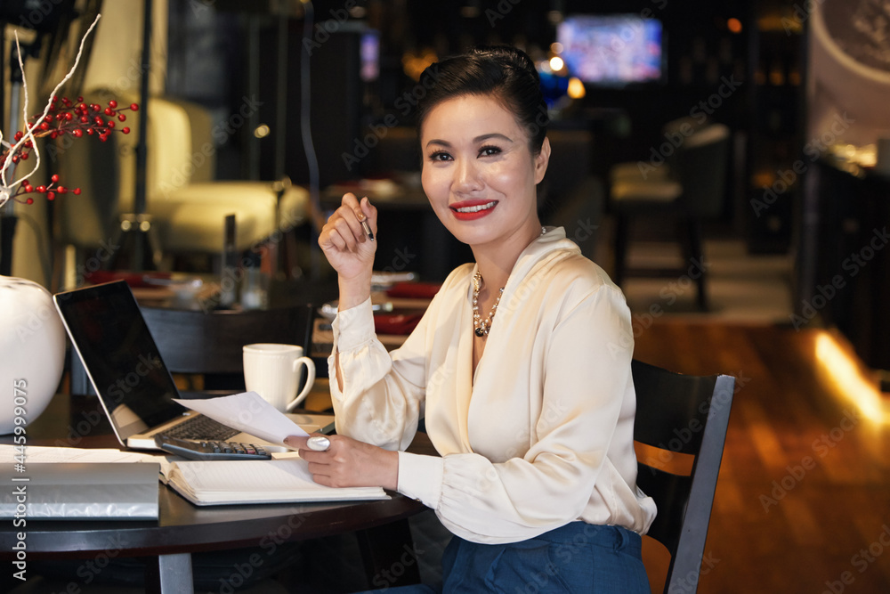 Portrait of beautiful smiling businesswoman working at restaurant table and signing documents