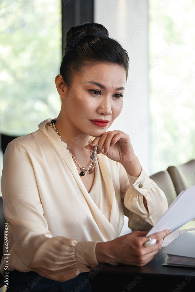 Serios pensive female entrepreneur reading document with important information Serios pensive female entrepreneur reading document with important information