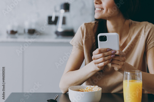 Billede på lærred Cropped up photo shot young housewife woman 20s in casual clothes t-shirt eat porridge use mobile cell phone look for recipe cook food in light kitchen at home alone