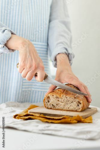 women's hands hold bread against the background of a light apron, a woman cuts bread, bread with a crispy crust is beautiful and appetizing, delicious bread lies on a wooden cutting board and a