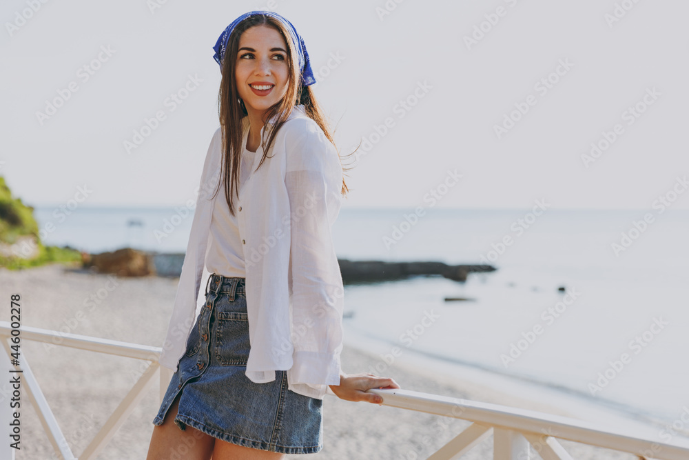 Smiling young stylish happy traveler tourist woman 20s wear blue bandana white shirt summer casual clothes standing resting outdoors at sea beach background People vacation lifestyle journey concept Smiling young stylish happy traveler tourist woman 20s wear blue bandana white shirt summer casual clothes standing resting outdoors at sea beach background People vacation lifestyle journey concept