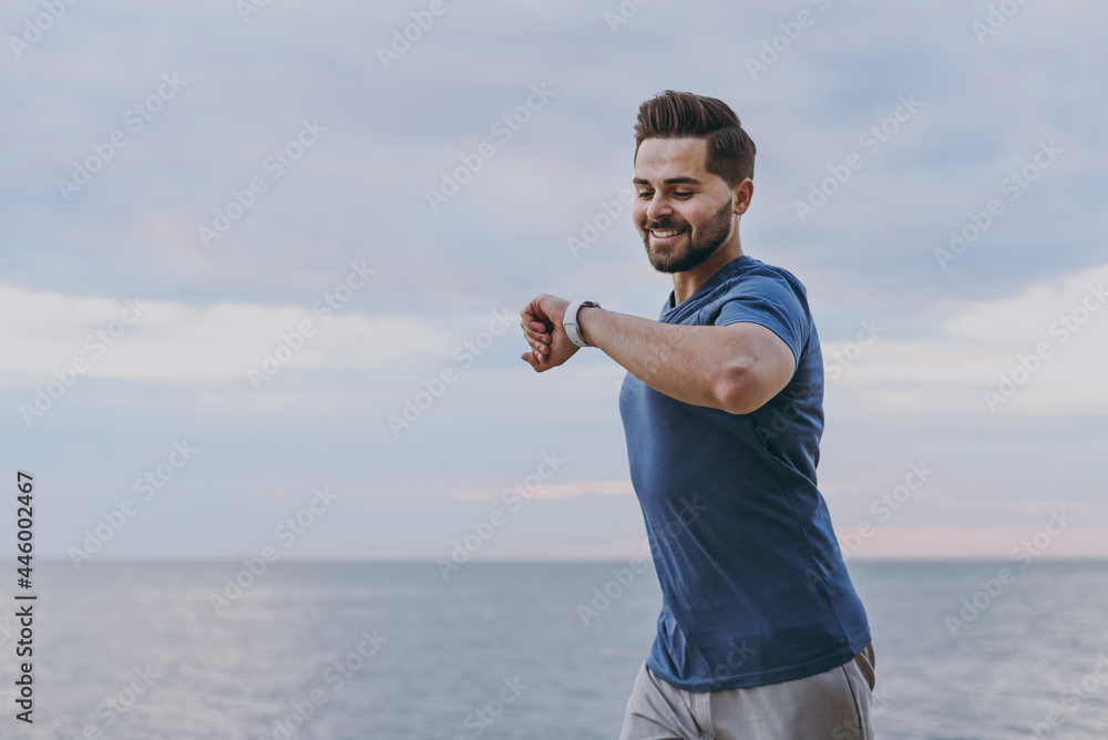 Top view young strong sporty fit sportsman man 20s wear sports clothes warm up training run look at smart watch using app at sunrise sun over sea beach outdoor on pier seaside in summer day morning Top view young strong sporty fit sportsman man 20s wear sports clothes warm up training run look at smart watch using app at sunrise sun over sea beach outdoor on pier seaside in summer day morning