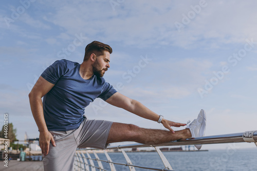 Young strong sporty athletic fit sportsman man in sports clothes warm up training tilt body sides hand stretch lunge exercise at sunrise over sea beach outdoor on pier seaside in summer day morning