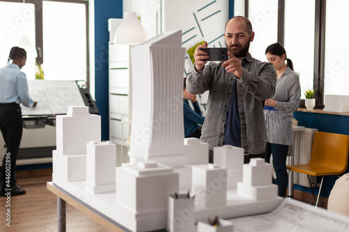 Architect profession man looking at maquette layout using smartphone to design building model plan maquette. Urban designer constructor working on professional modern construction