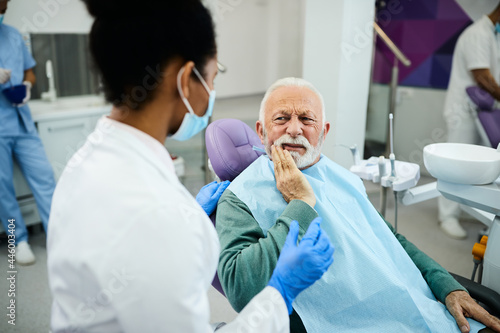Mature man with toothache talking to dentist during appointment at dental clinic.