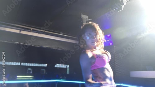 Close-up of a girl in underwear dancing to the beat of the music with her hands. She is dressed in pink underwear and is surrounded by club floodlights.