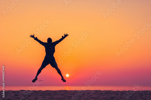 Man jumping on tropical beach with sunset sky and island background. Freedom and feel good concept.
