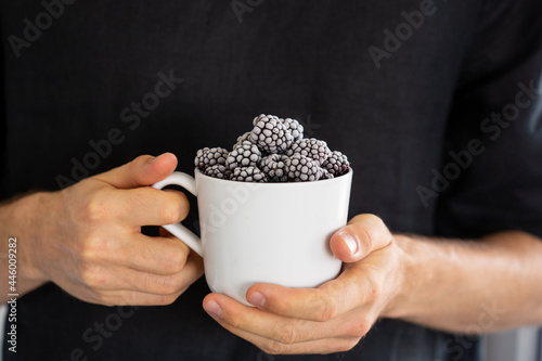 Frozen blackberries in a cup holding in two hands. White male with organic berries. photo