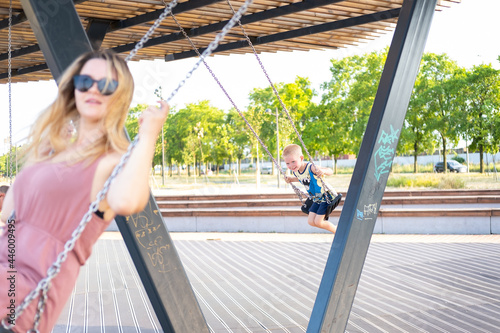 adult caucasian modern woman mom with son swinging on a swing in the playground. happy girl on a swing © yana136