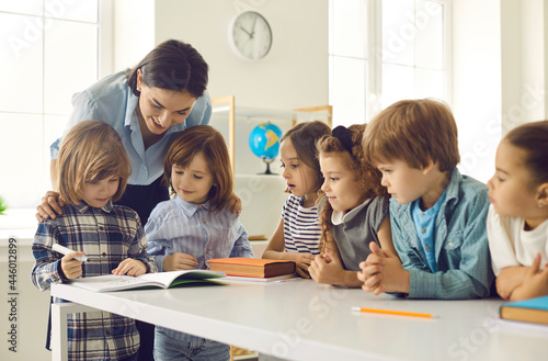 Little school children learning to write. Happy kids acquiring new skills in class. Young school teacher helping her cute little students who are writing in their notebooks or activity books