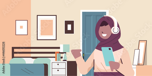 arabic schoolgirl using smartphone and listening to music in headphones arab girl with gadget relaxing at home