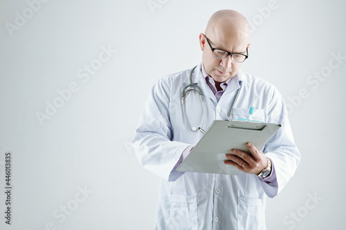 Mature doctor in white coat making notes in medicl card standing against the white background photo