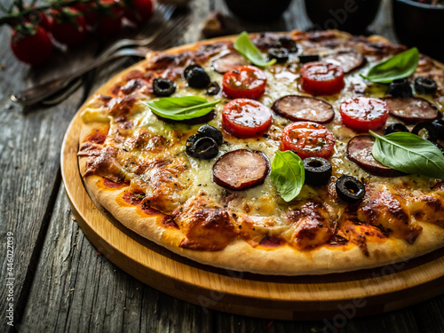 Pizza with white mushrooms  sausage  tomatoes  black olives  parmesan and mozzarella on wooden background 