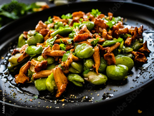 Obraz na płótnie Broad beans salad with fried chanterelles, garlic and parsley on wooden table