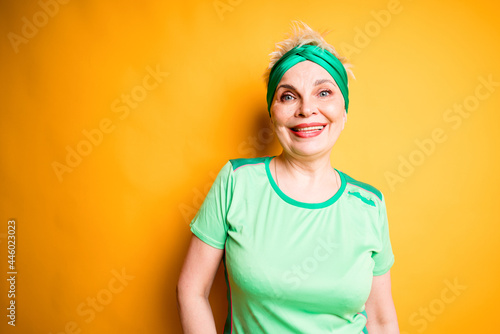 Cheerful woman in sportswear smiling broadly while standing on yellow background and going to the gym