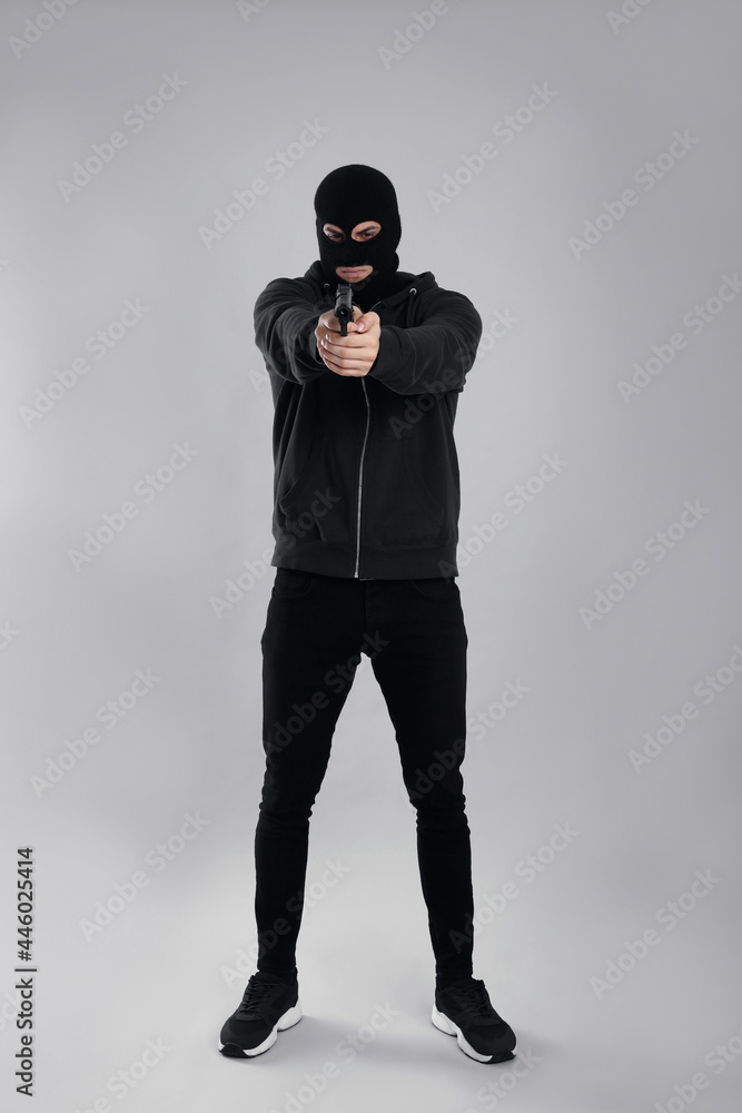 Man wearing black balaclava with gun on light grey background Man wearing black balaclava with gun on light grey background