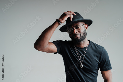 Handsome african american man in glasses and in a hat touches her with his hand smiling and standing on a gray background