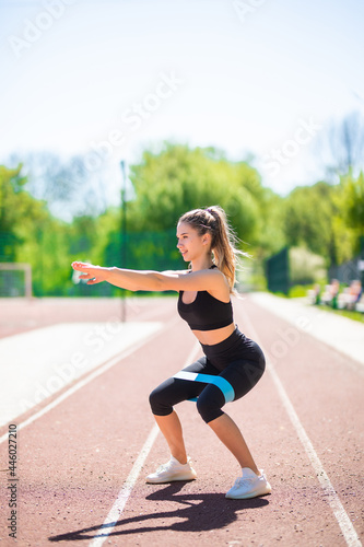 Young attractive athletic sportswoman make exercises with elastic band on outdoors stadium