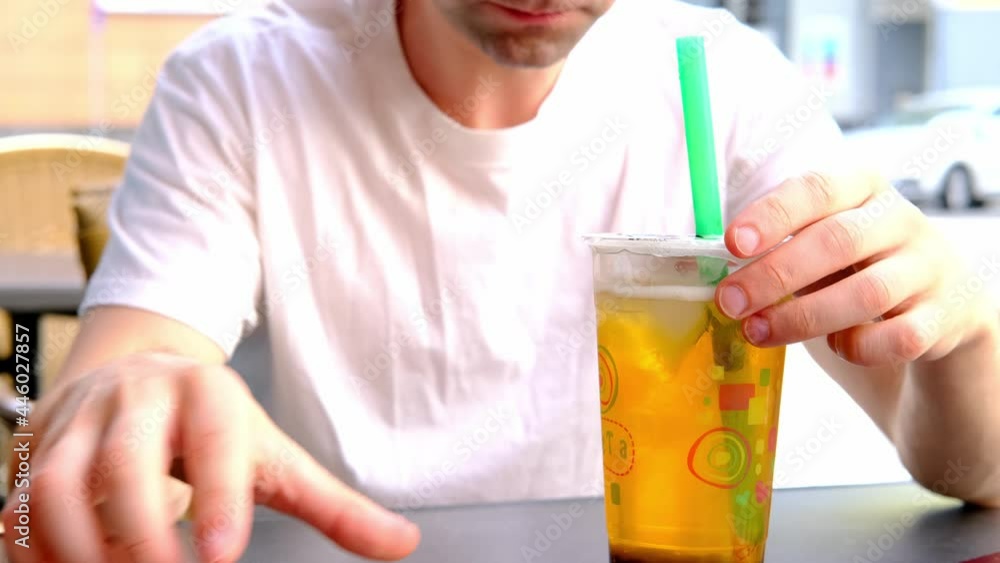 positive young man in white t-shirt close-up sitting in street cafe in summer, drinking from glass of bubble tee, bright light of sun concept of vacation, tourist travel, summer vacation, summermood positive young man in white t-shirt close-up sitting in street cafe in summer, drinking from glass of bubble tee, bright light of sun concept of vacation, tourist travel, summer vacation, summermood