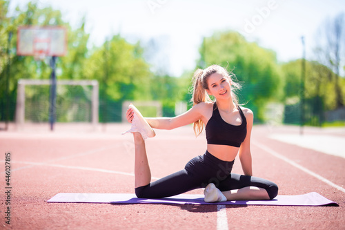Attractive young sportive woman doing yoga stretching thighs outside on the mat.