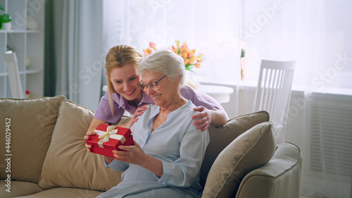 Fotografía Long haired blonde in purple dress gives small box with present to aged lady