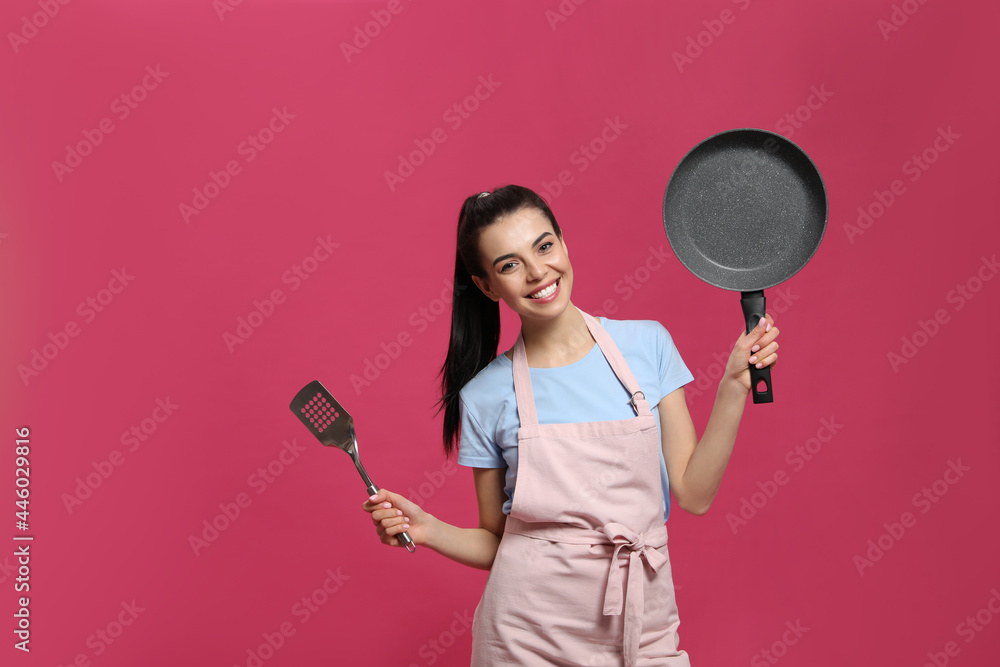 Housewife with frying pan and spatula on pink background. Space for text Housewife with frying pan and spatula on pink background. Space for text