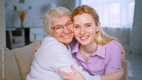 Happy girl and elderly woman embracing and looking at the camera