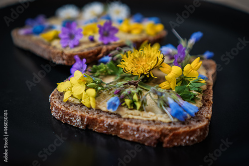 vegan cream cheese substitute on a whole grain bread slice or toast which is flowery decorated with Red clover  dandelion and meadow flowers for a healthy breakfast or snack