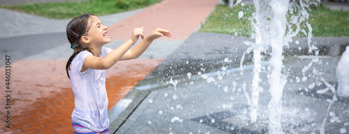 Funny little girl in the fountain plays with splashes of water.