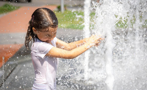 Fototapeta Naklejka Na Ścianę i Meble -  Funny little girl in the fountain plays with splashes of water.