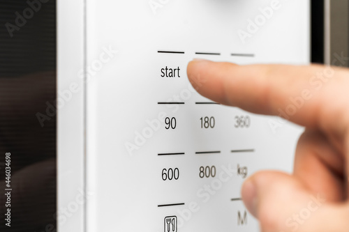 Hand pushing button of microwave oven for cooking food in kitchen