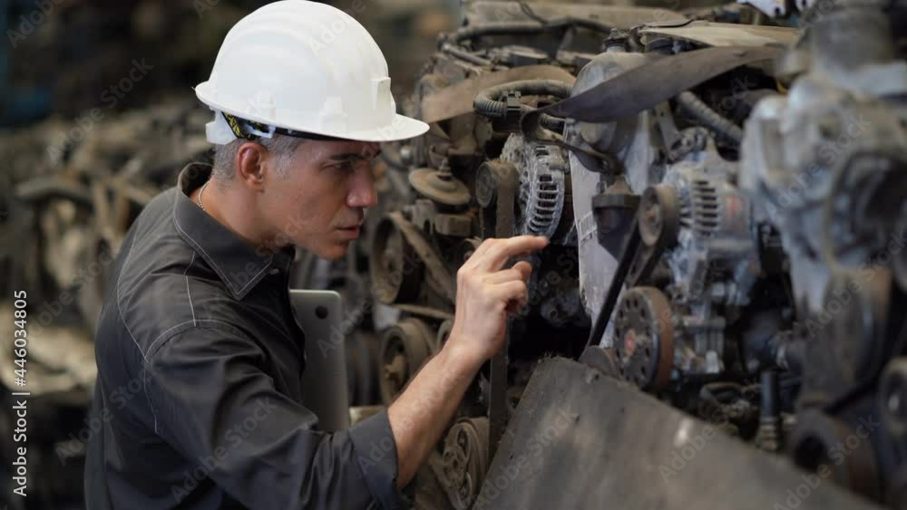 senior engineer using laptop computer checking list old used car engine in machinery parts shop warehouse. old technician man Repair vehicle automobile machine in Recycle motor factory senior engineer using laptop computer checking list old used car engine in machinery parts shop warehouse. old technician man Repair vehicle automobile machine in Recycle motor factory