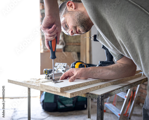 A man is screwing in a screw, a self-tapping screw for wood.