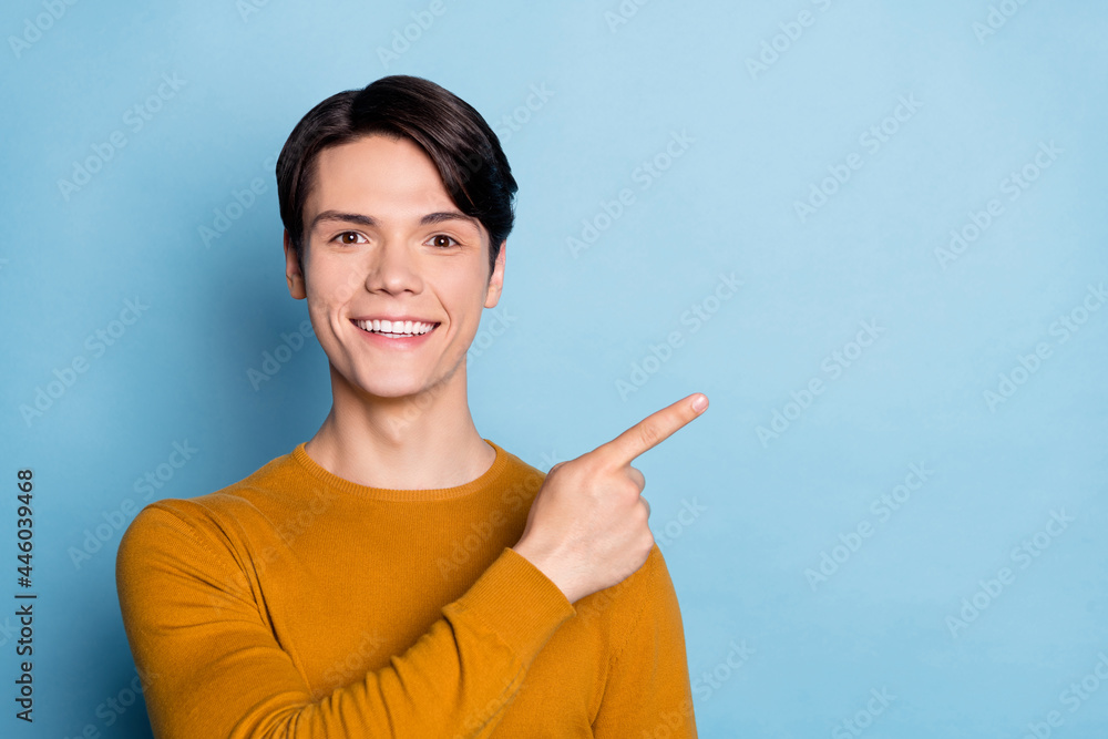 Photo of young guy happy positive smile point finger empty space advertise promo isolated over blue color background Photo of young guy happy positive smile point finger empty space advertise promo isolated over blue color background
