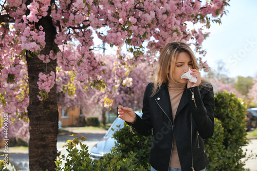 Woman suffering from seasonal pollen allergy near blossoming tree outdoors photo