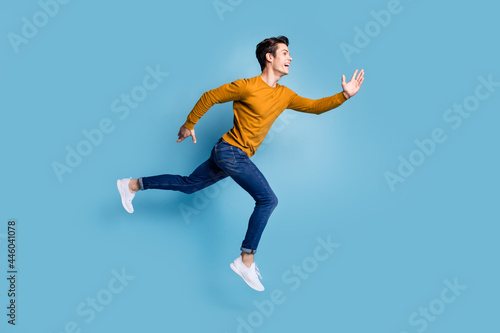 Full length profile photo of funny brunet young guy run wear sweater jeans isolated on blue color background