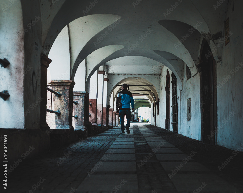 arcade passageway in small town, walking man seen from behind