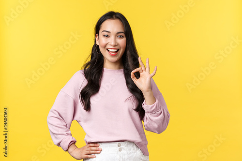 People emotions, lifestyle and fashion concept. Impressed and excited smiling asian woman totally agree with you, showing okay sign and nod approval, standing yellow background photo